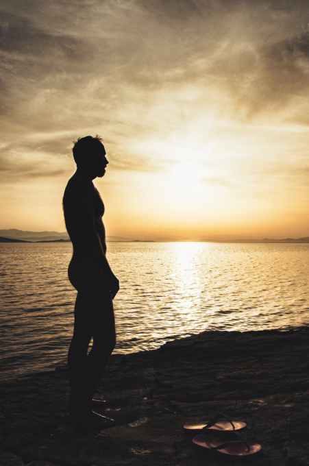 topless man on sand near body of water during sunset