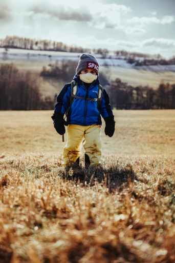 kid in blue jacket and brown pants walking on brown grass field