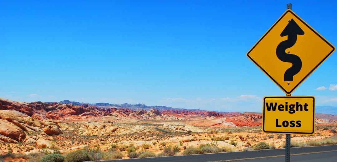 road sign with a desert in the background. sign shows a cure road and reads weight loss